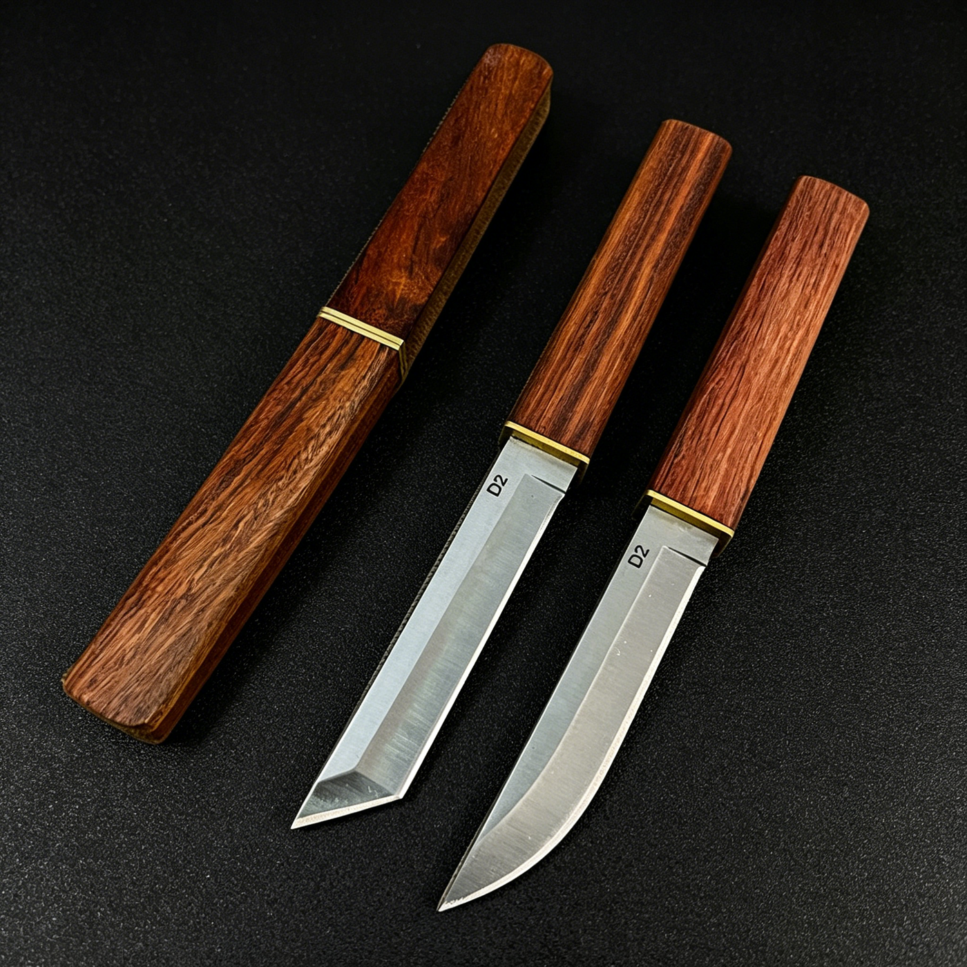 An empty wooden sheath on the left, and two D2 steel fixed blade knives with wooden handles and brass accents on the right. One features a tanto-style blade, and the other features a curved blade, displayed on a dark textured surface.