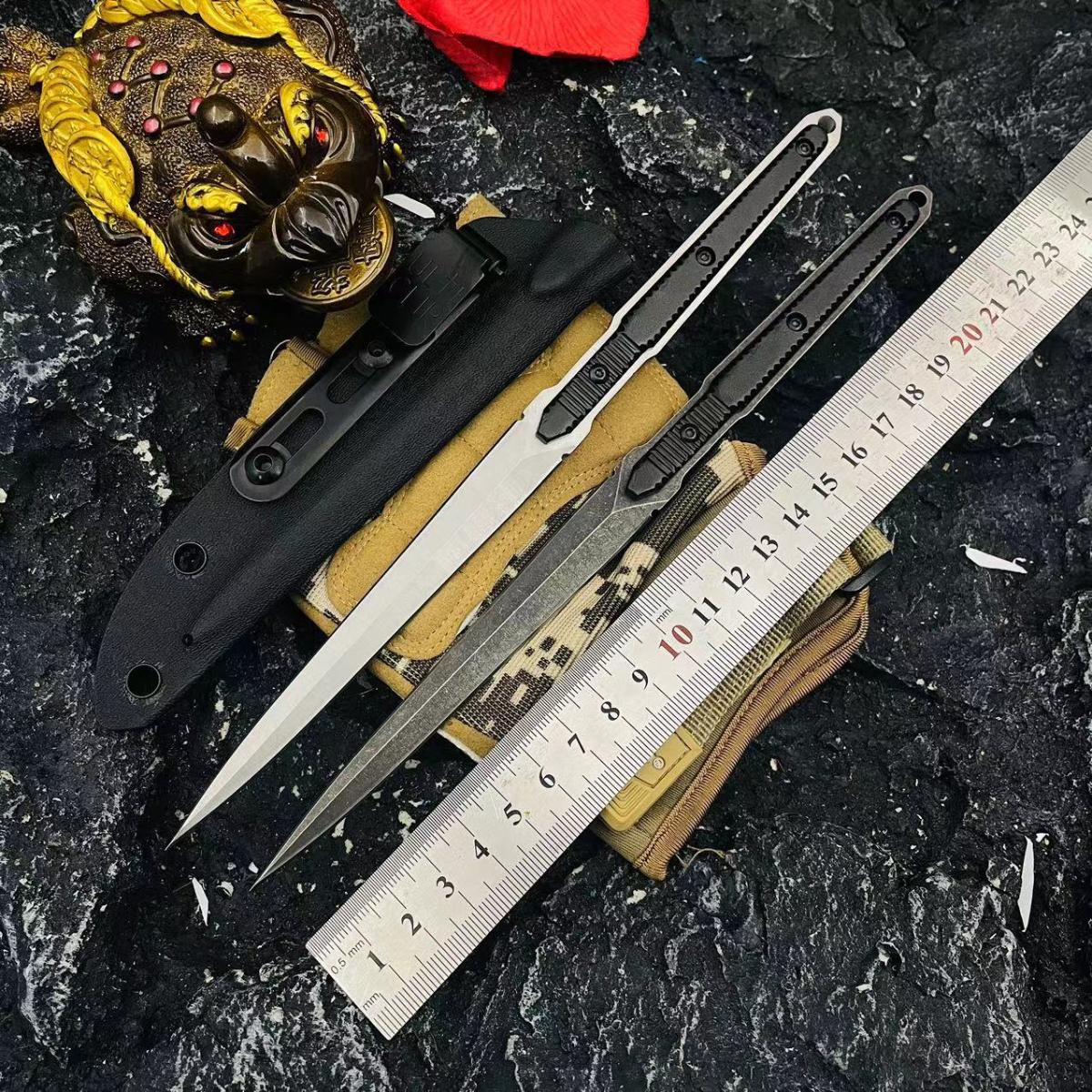 A tactical layout of two slim folding knives with black and silver blades, displayed with a black sheath, black pouch, metal ruler for size reference, and decorative props on a dark rocky background.