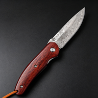 An open folding knife with a patterned damascus steel blade and a polished red wooden handle, featuring a brown lanyard at the end, displayed on a dark textured surface.