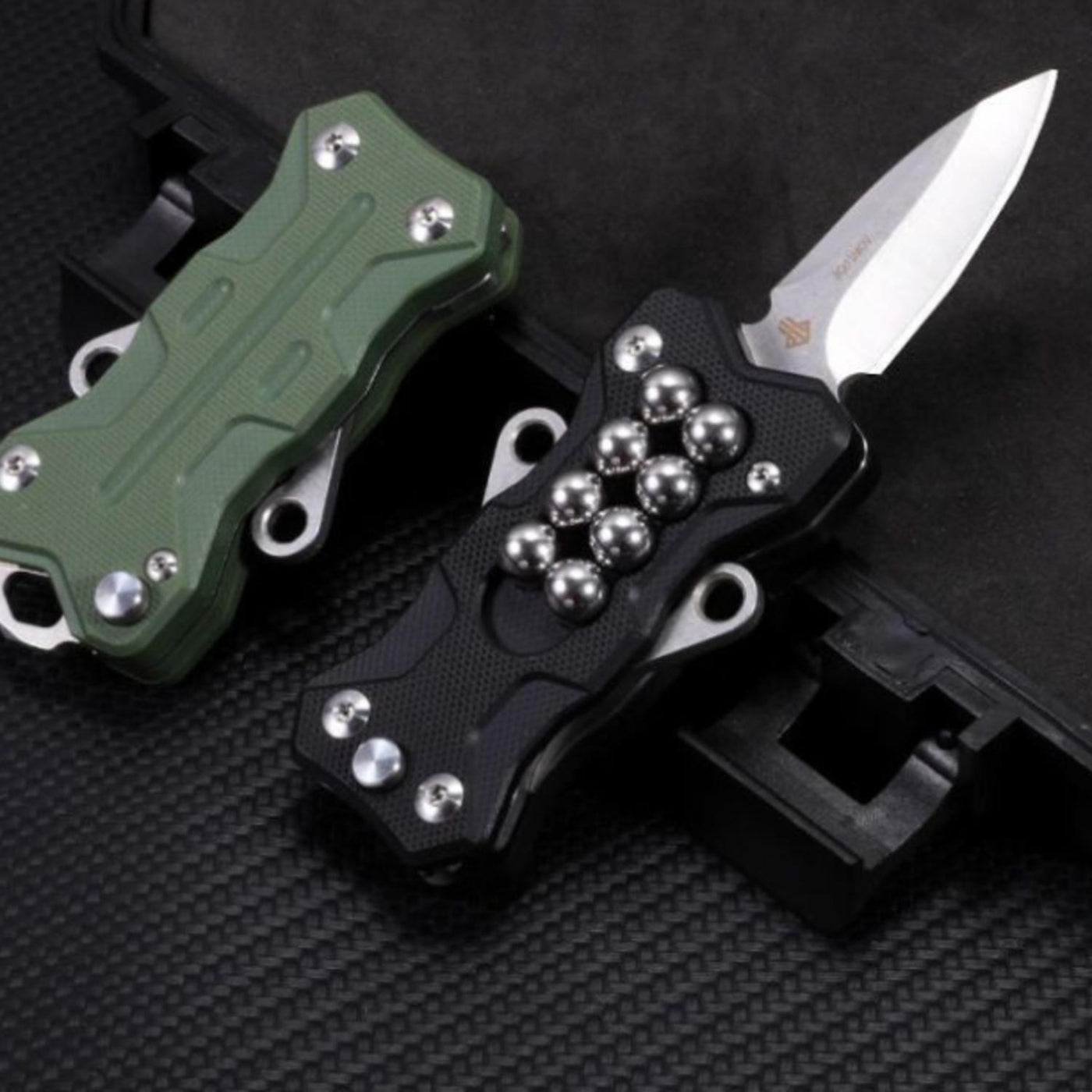 Two EDC multi-tool slingshots, one in green and one in black with the knife blade deployed, displayed on a dark background.