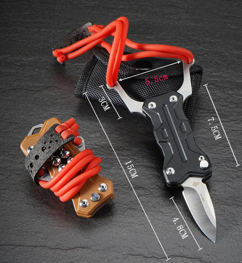 A dimension specification chart for the EDC slingshot knife, showing measurements including an overall length of 15cm, a 4.8cm blade, a 7.5cm handle, and a 5.5cm fork width, displayed with a black sheath and a tan folded slingshot on a dark stone surface.