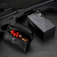 A product packaging display showing a tan EDC slingshot with red bands tucked inside a black nylon pouch, placed next to its black and silver APEXT brand packaging box, all set against a dark tactical background.
