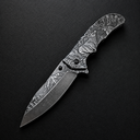 An open folding knife featuring intricate engraving of a deer and forest landscape on the blade and handle, displayed on a dark textured surface.