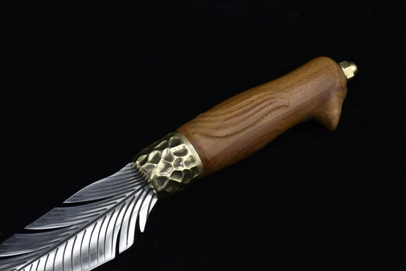 A detailed close-up of the hammered brass bolster and the carved wooden handle of an engraved feather blade fixed knife, displayed on a dark background.