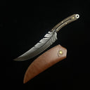 A custom fixed blade knife with a silver feather-engraved blade and a dark wood handle with brass pins, displayed next to its brown leather sheath with a brass snap button, on a black background.