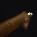 A close-up of the wooden handle and brass pommel of an engraved feather blade fixed knife, displayed on a dark background.
