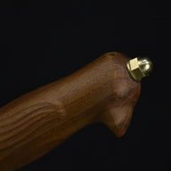 A close-up of the wooden handle and brass pommel of an engraved feather blade fixed knife, displayed on a dark background.