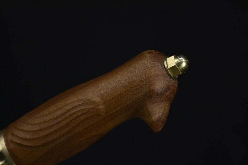 A close-up of the wooden handle and brass pommel of an engraved feather blade fixed knife, displayed on a dark background.