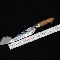 An open fixed knife with a silver feather-patterned blade and a hammered brass bolster, displayed on a dark background with a metal ruler and a plastic protractor to show its dimensions and blade angle.