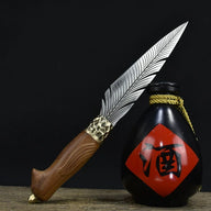 An engraved feather blade fixed knife with a wooden handle and brass bolster, displayed diagonally next to a black liquor gourd with a red diamond label on a dark background.