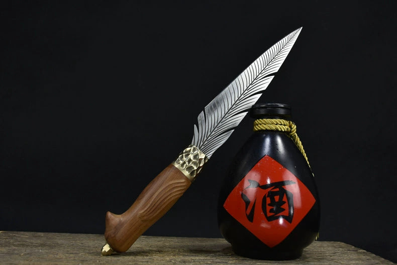 An engraved feather blade fixed knife with a wooden handle and brass bolster, displayed diagonally next to a black liquor gourd with a red diamond label on a dark background.