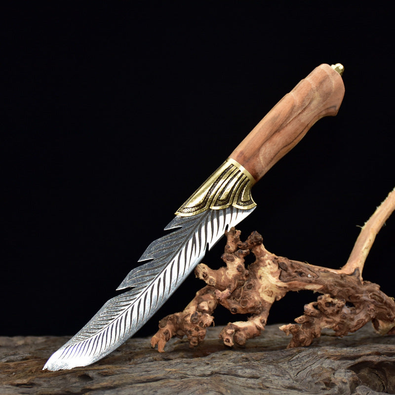 An engraved feather blade knife with a brass bolster and wooden handle, displayed next to a decorative wooden carving on a dark background.