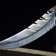 A close-up of the curved silver blade of a custom fixed knife, highlighting the intricate feather engraving, displayed next to a black liquor gourd.
