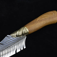 A close-up view of a fixed blade knife showing the ridged brass bolster and polished wooden handle with a decorative brass end cap.