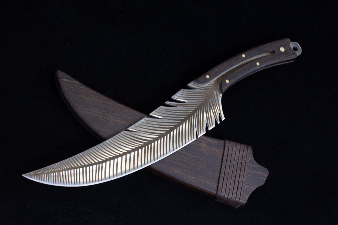 An engraved feather blade knife crossed over its dark wooden sheath, displaying the matching wood grain on the handle and sheath.