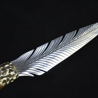 A close-up view of a custom fixed blade knife, capturing the light reflections on the intricate feather-patterned silver blade and the textured brass bolster.
