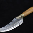 A full side view of a curved fixed blade knife with a feather-patterned blade, a ridged brass bolster, and a polished wooden handle, displayed on a dark background.