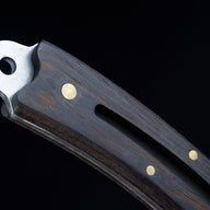A macro shot of the knife's silver lanyard hole pommel and the rich grain of the dark wood handle.