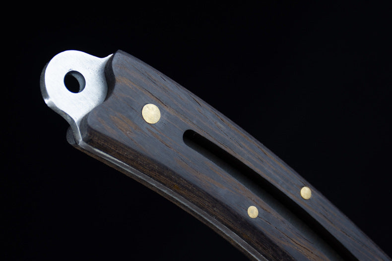 A macro shot of the knife's silver lanyard hole pommel and the rich grain of the dark wood handle.