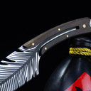 A close-up of the feather blade knife resting its handle on top of the black liquor gourd, highlighting the blade and handle design.