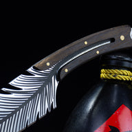 A close-up of the feather blade knife resting its handle on top of the black liquor gourd, highlighting the blade and handle design.