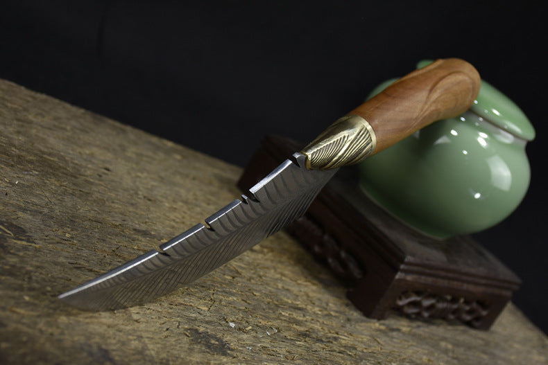 A side view of a custom fixed blade knife resting on a textured wooden board, highlighting the curved blade, brass bolster, and wooden handle.