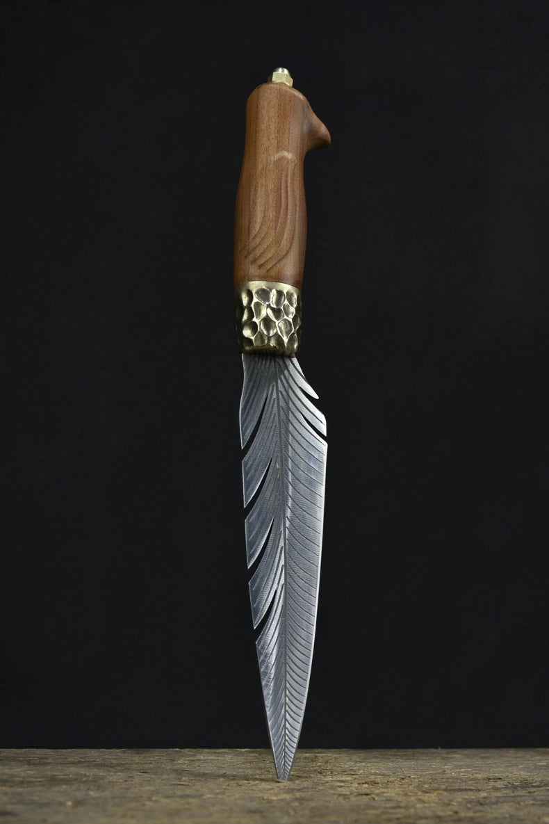 A handmade fixed blade knife with a grooved wooden handle and a hammered brass bolster, standing vertically on a dark surface.