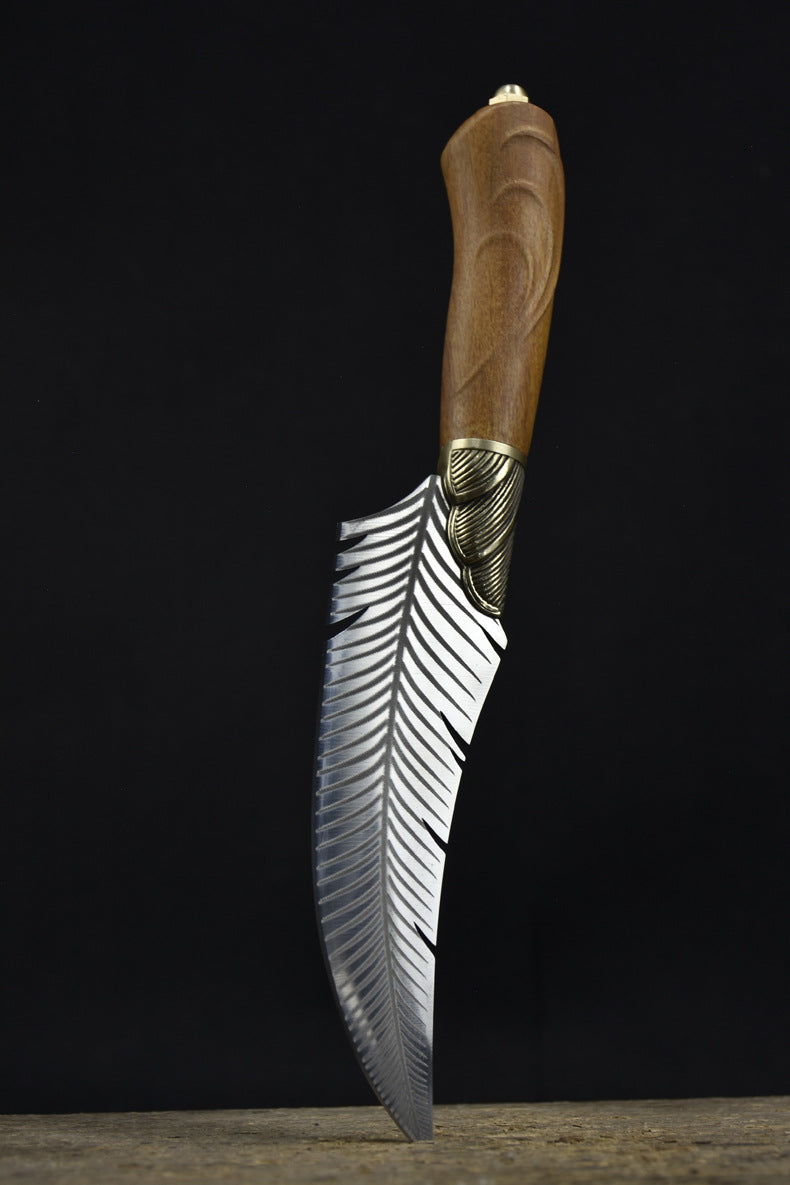 A handcrafted curved feather blade knife standing vertically on a wooden surface with its tip pointing downwards, displaying the handle and brass bolster against a dark background.