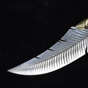 A close-up of an engraved fixed blade knife showing the intricate feather pattern and ridged brass bolster details against a dark background.