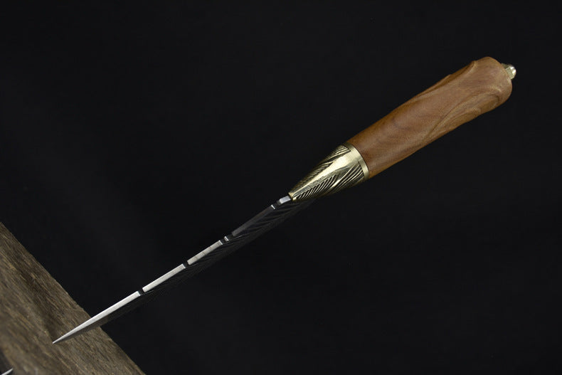 A close-up of the rear section of the blade on a custom fixed knife, highlighting the transition from the brass bolster to the detailed feather engraving.