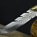 A close-up of the tip of an engraved silver feather blade, showcasing the curved shape and detailed feather engraving.