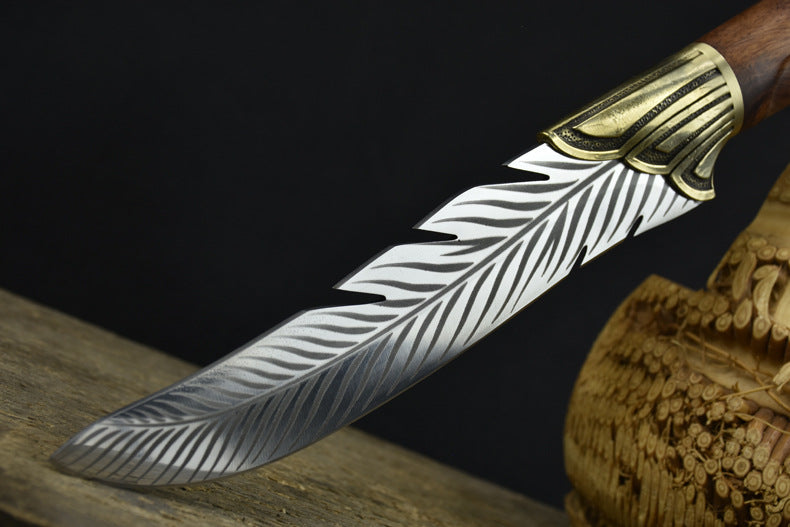 A close-up of the tip of an engraved silver feather blade, showcasing the curved shape and detailed feather engraving.