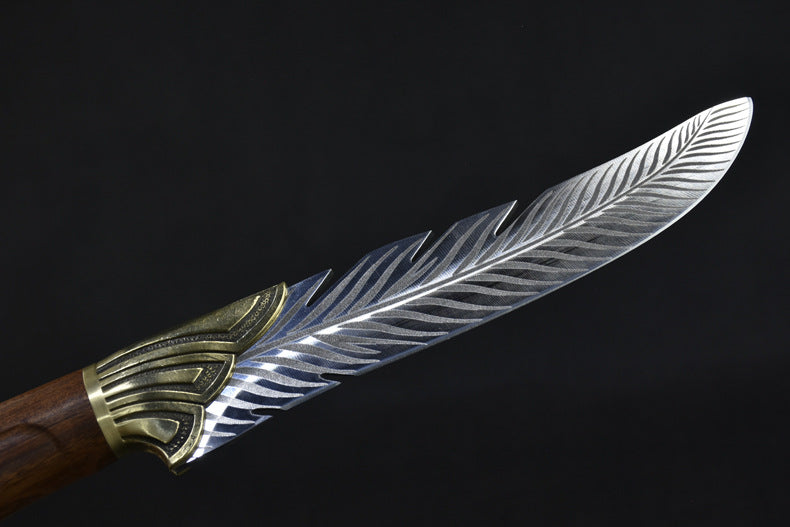 A close-up highlighting the curved edge and layered feather pattern engraving on the silver blade of a fixed knife.