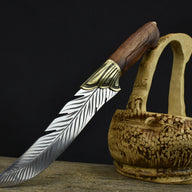 An engraved feather blade knife with a brass bolster and wooden handle, displayed next to a finely carved hollow wooden basket.