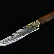 An open fixed blade knife featuring an engraved feather-patterned silver blade and a wooden handle, displayed horizontally on a black background.