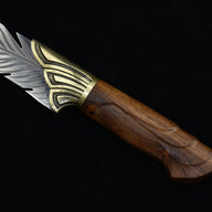 A close-up of the silver blade of an engraved feather knife, showcasing the detailed feather textures, with the wooden handle partially visible.