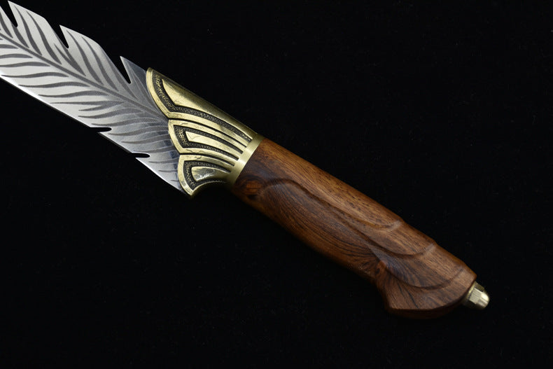 A close-up of the silver blade of an engraved feather knife, showcasing the detailed feather textures, with the wooden handle partially visible.