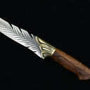 A close-up of the wooden handle and textured brass bolster of a feather-blade fixed knife, displayed on a black background.