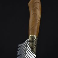 A close-up view of the carved wooden handle and brass pommel of a custom fixed blade knife, showcasing the natural grain and brass hardware details.