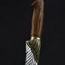 A close-up of the polished wooden handle and brass bolster of a custom feather blade knife.