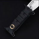 A close-up of a folding knife featuring a textured black handle with finger grooves and a gold pivot button, paired with a silver blade that includes a fuller, displayed on a dark background.