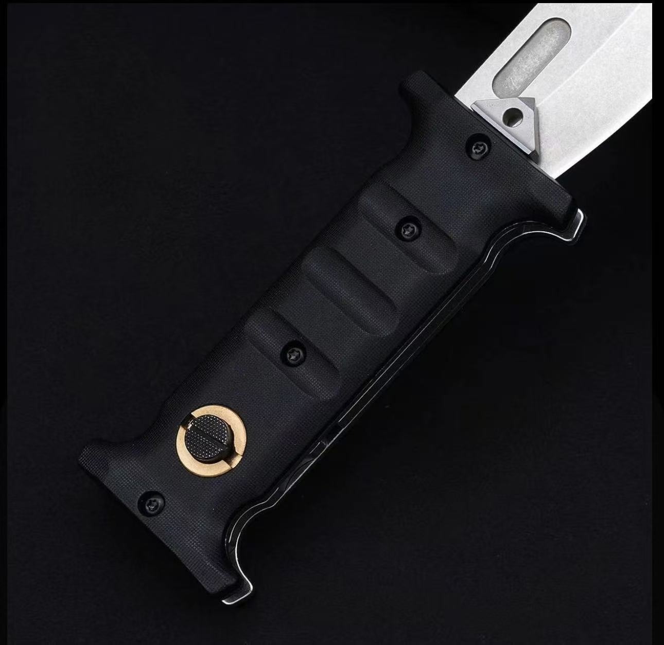 A close-up of a folding knife featuring a textured black handle with finger grooves and a gold pivot button, paired with a silver blade that includes a fuller, displayed on a dark background.