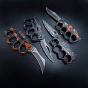 A collection of four open knuckle duster folding knives with various custom graphic handles including skulls and different blade styles, displayed on a dark background.