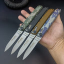 An open hand holding four folding knives with various camo and solid-colored handles, showing their compact size.