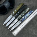 Four open folding knives with different colored handles displayed with a metal ruler and a black goggle on a textured leather surface.
