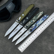 Four open folding knives with different colored handles displayed with a metal ruler and a black goggle on a textured leather surface.