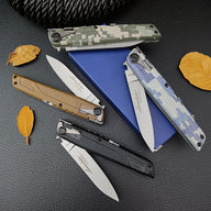 Two open and two closed folding knives scattered on a blue rectangular box lid, surrounded by yellow dried leaves on a dark surface.