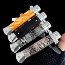 Four closed stiletto knives with different handle styles—orange resin, black, and snakeskin textures—held in a hand against a dark background.