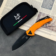 An open folding knife with a black blade and an orange textured handle, featuring a star logo, displayed next to a black nylon pouch with a fox logo and Italian flag stripe, resting on vintage printed paper on a dark textured surface.