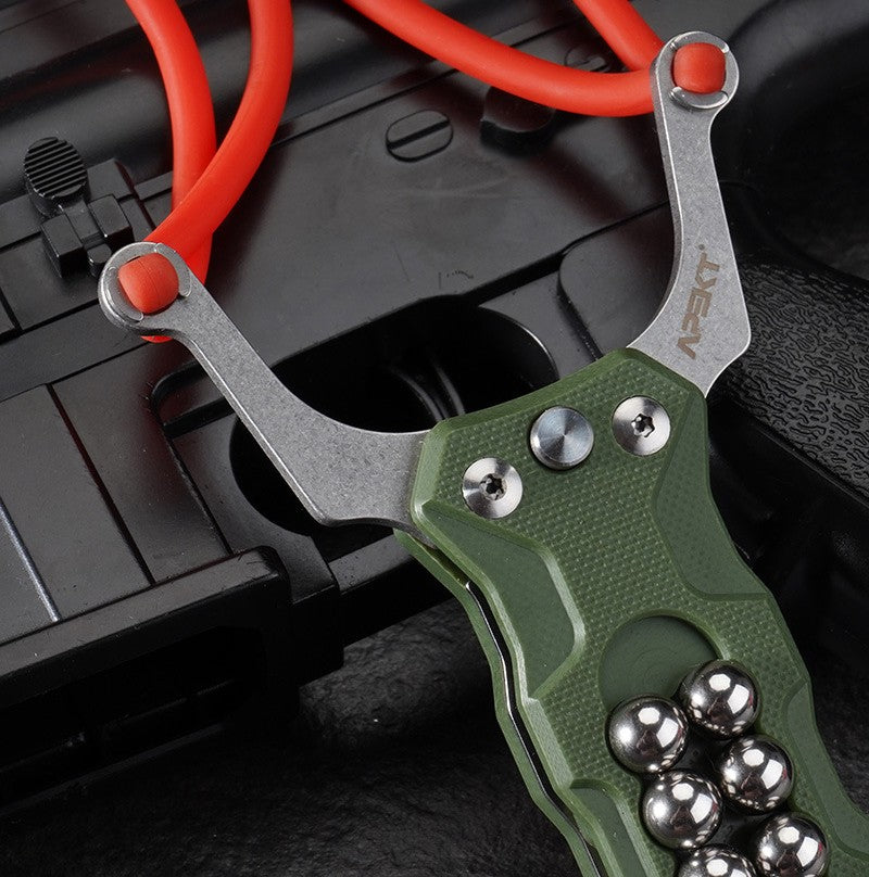 A close-up view of a green G10 handle EDC slingshot, highlighting the stainless steel fork, the red rubber band attachment, and the embedded steel ball storage, displayed on a dark tactical background.